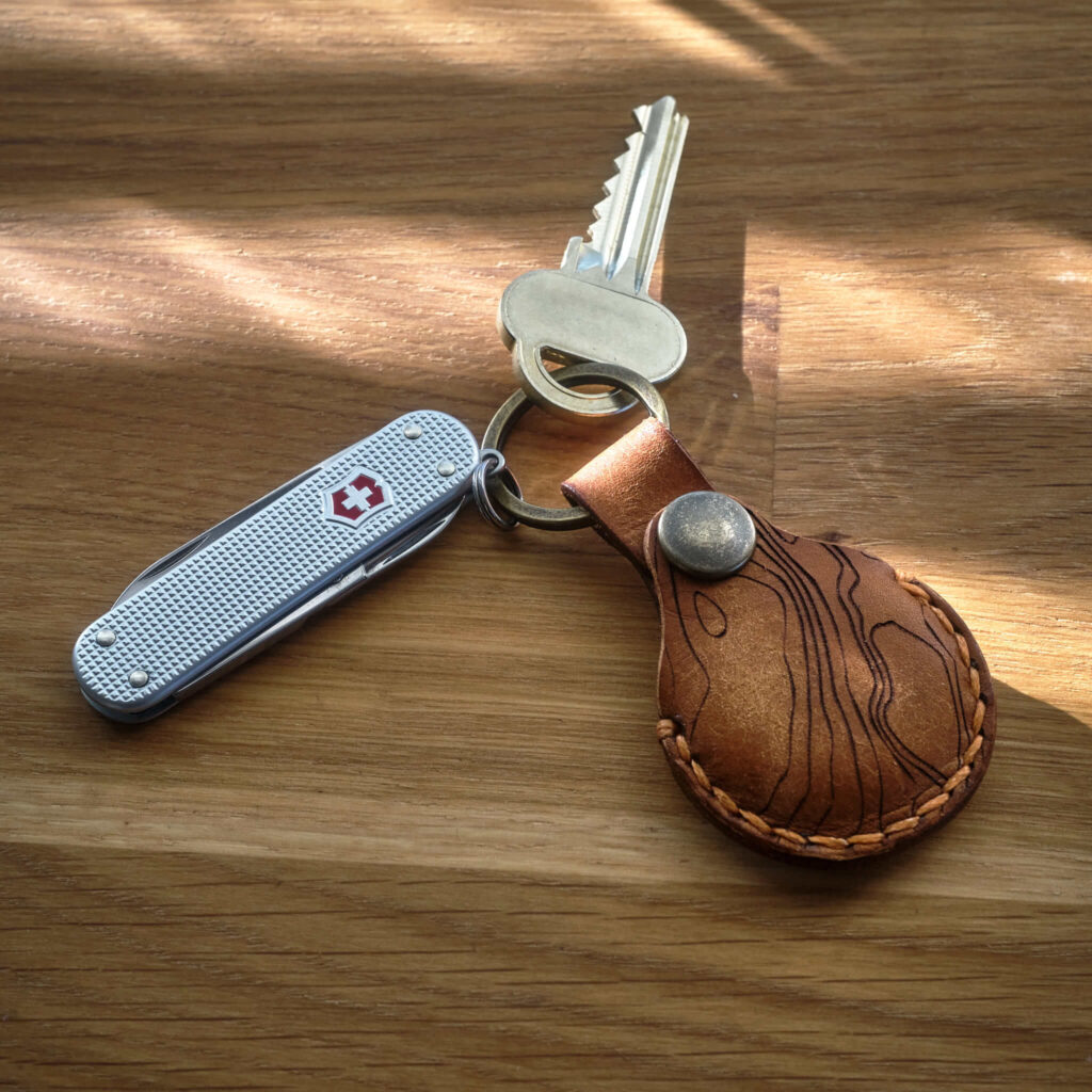 Victorinox Classic Alox med en handsydd brun Apple AirTag nyckelring i läder med topografiskt mönster som är tillverkad i Sverige.