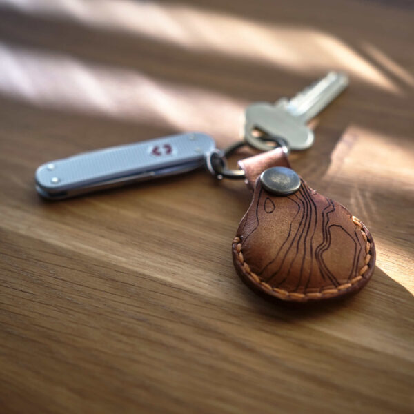 Nyckelknippa med en handsydd brun Apple AirTag nyckelring i läder med topografiskt mönster som är tillverkad i Sverige. Samt Victorinox Classic Alox.