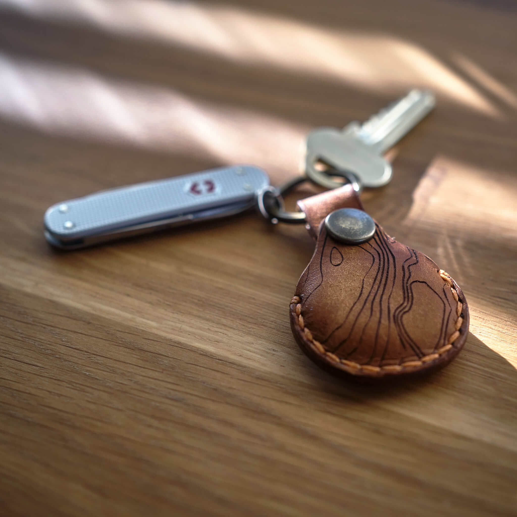 Nyckelknippa med en handsydd brun Apple AirTag nyckelring i läder med topografiskt mönster som är tillverkad i Sverige. Samt Victorinox Classic Alox.
