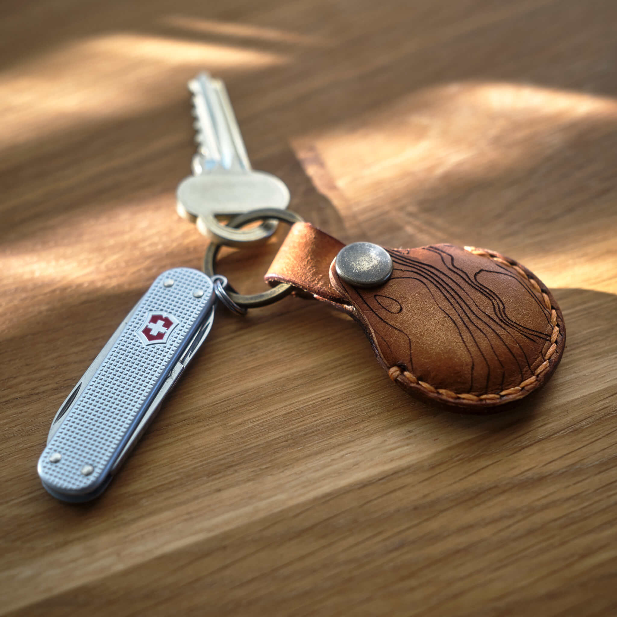 Victorinox Classic Alox med handsydd brun Apple AirTag nyckelring i läder med topografiskt mönster som är tillverkad i Sverige.