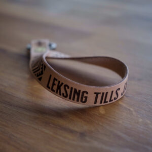 Nyckelring med läderrem med ett egenkomponerat krusbandsmönster samt texen Leksing tills jag dör. Tillverkade i Sverige.
