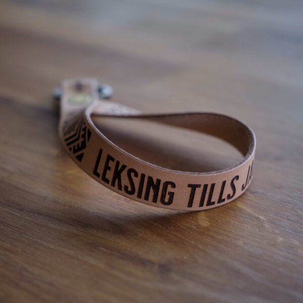 Nyckelring med läderrem med ett egenkomponerat krusbandsmönster samt texen Leksing tills jag dör. Tillverkade i Sverige.