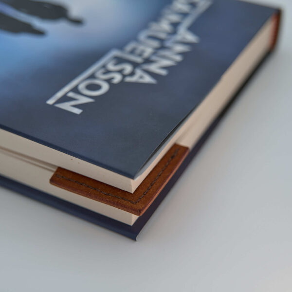 Bokmärke i läder tillverkad av vegetabiliskt garvat ljusbrunt läder och färgmatchad tråd. Här ser man hur den används i en bok. Tillverkad i Sverige.