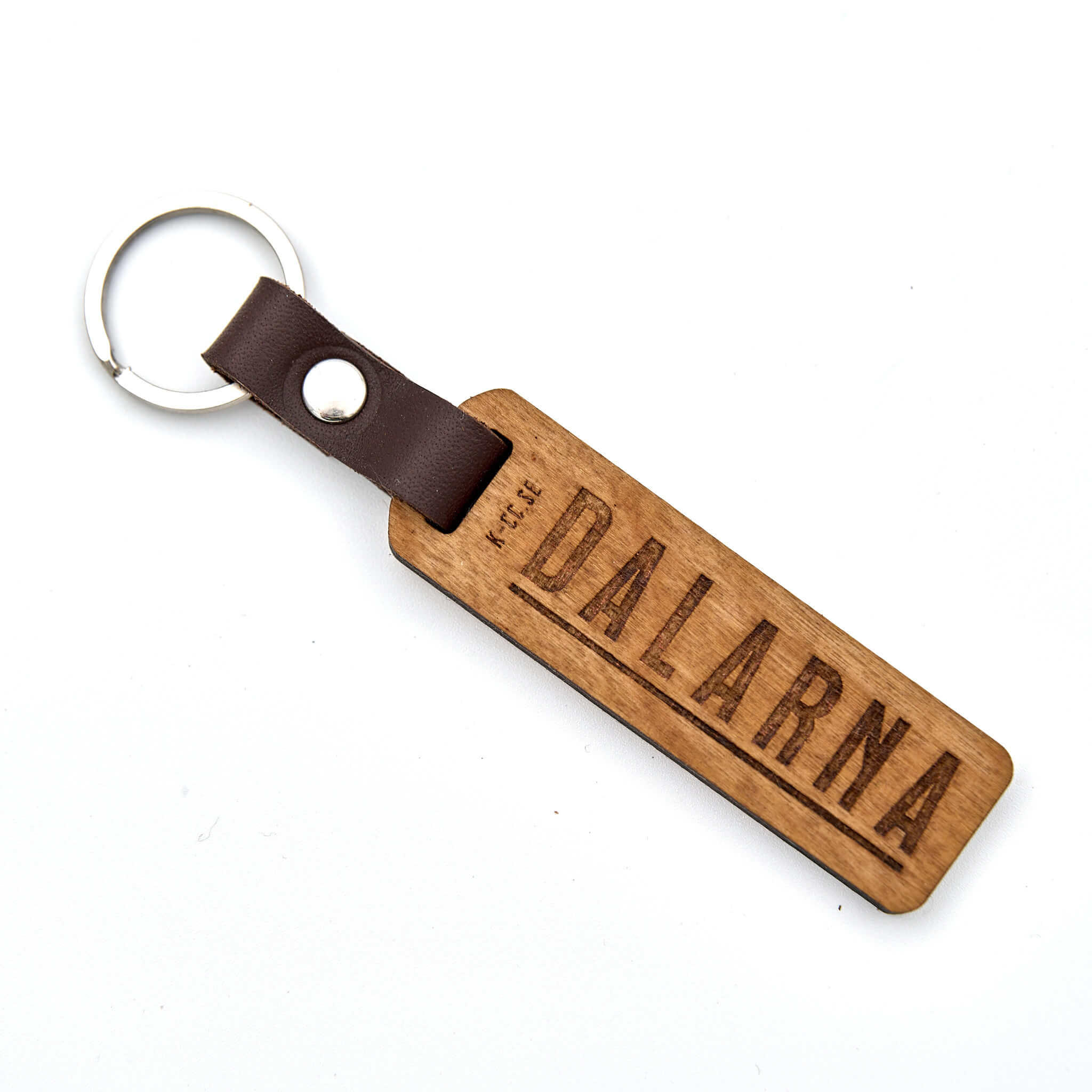 Nyckelring med texten DALARNA. Tillverkad av björkplywood. En bit vegetabiliskt garvat läder binder ihop det hela mot nyckelringen. Tillverkad här i Sverige.