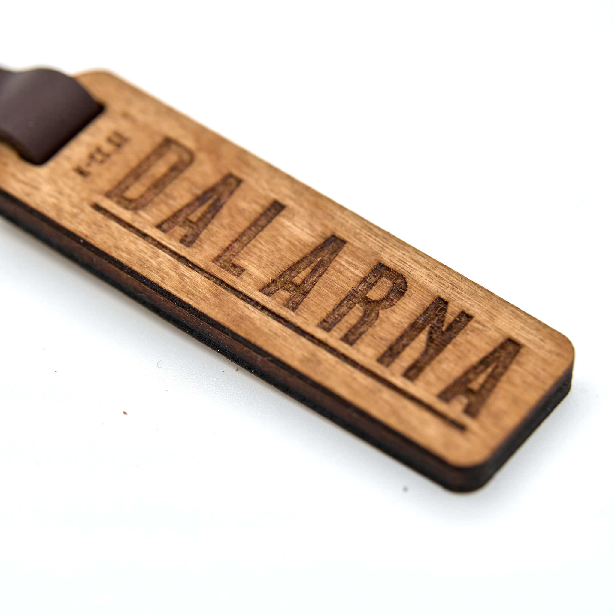 Nyckelring med texten DALARNA. Tillverkad av björkplywood. En bit vegetabiliskt garvat läder binder ihop det hela mot nyckelringen. Tillverkad här i Sverige.